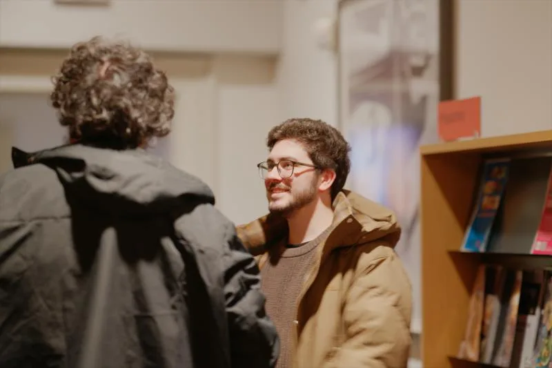 Gallery image: 01 talking 09 july chatting by the bookshelves.webp